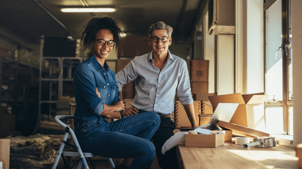 Two entrepreneurs smiling in their warehouse, illustrating business loans that help owners with bad credit start or grow their businesses.