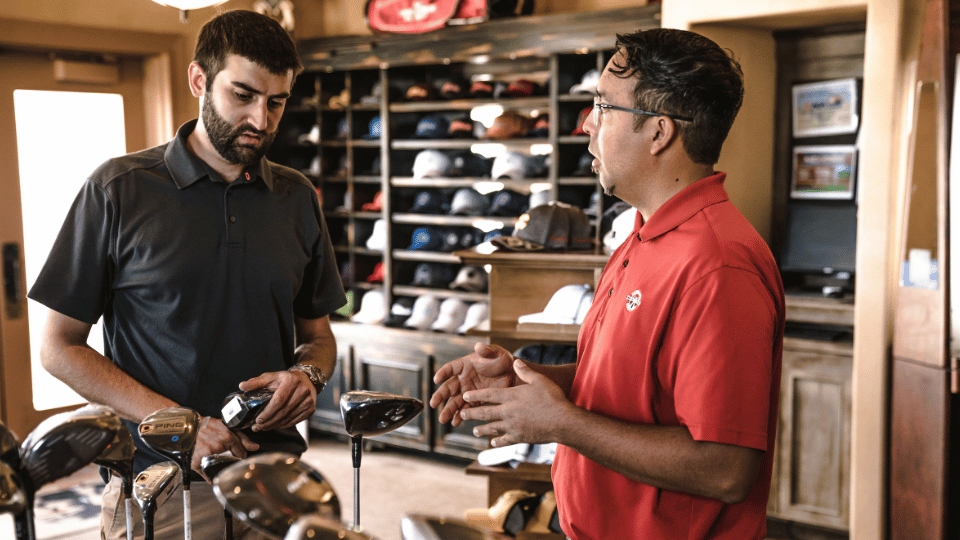 Un vendedor hablando con un cliente sobre los tipos de palos de golf