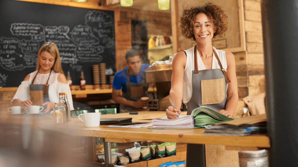 Smiling café owner managing paperwork, representing small business owners exploring alternative financing options.