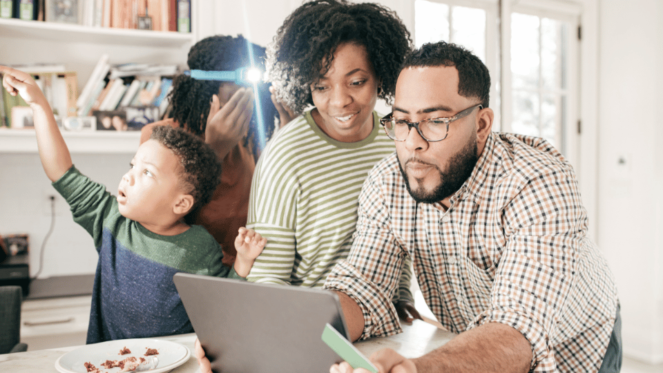 A family gathered around a laptop, with the father making an online purchase while the child points excitedly. The image illustrates creating urgency in sales, encouraging immediate action from customers, such as limited-time offers or flash sales.