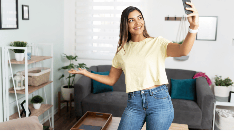 A smiling woman taking a selfie in her living room, representing an influencer creating content. The image illustrates how small businesses can leverage social proof through influencer marketing to boost sales.