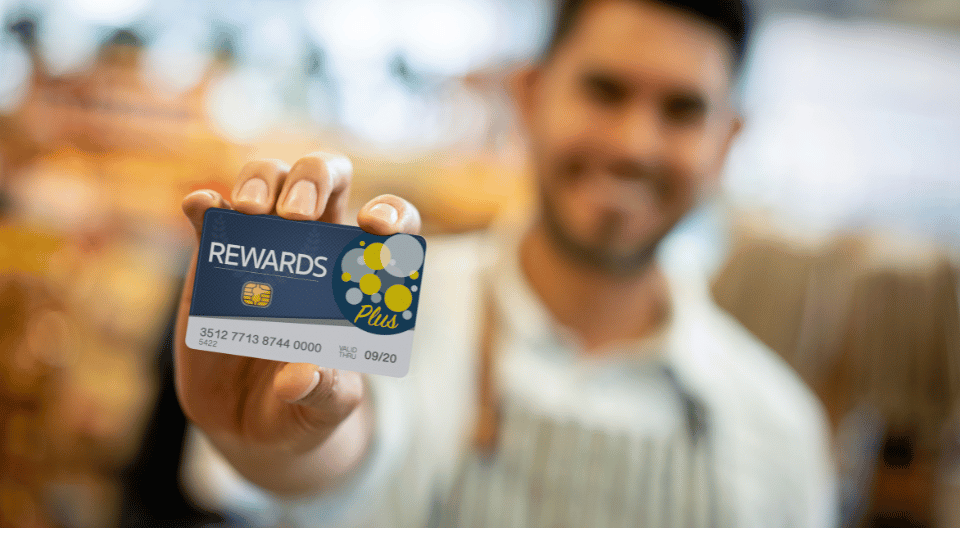 A smiling man holding up a rewards card, symbolizing a customer loyalty program. The image highlights the concept of encouraging repeat business through loyalty incentives.