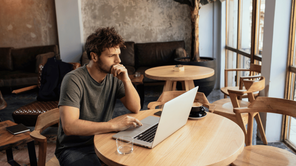 A thoughtful man working on his laptop in a cozy cafe, symbolizing the careful consideration needed when learning about different types of business ownership.